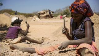 Женщина и ребенок разбивают камни из кобальтовой шахты