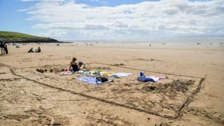 A woman sits alone in an area marked in the sand on Barry Island beach, Wales.