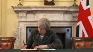 Theresa May oo saxeexaysa warqadii rasmiga ahayd ee Midowga Yurub lagu ogaysiinayey in dalkeedu ka baxay midowga