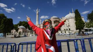 Una mujer envuelta en una bandera nacional turca gesticula afuera del museo de Hagia Sophia el 10 de julio de 2020 en Estambul mientras la gente se reúne para celebrar después de que una corte superior de Turquía revocó la Hagia Sophia del siglo VI.