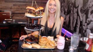 Kate Ovens is professional food challenge blogger, sitting in front of a giant platter of food.