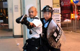 A police officer points a gun towards anti-extradition bill protesters