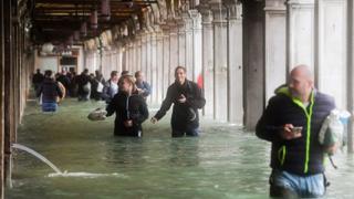 Tourists walk to flooded St. Mark's Square in Venice on October 29, 2018