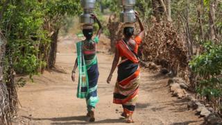 Women carry pitchers after filling them with water from a hand pump to their houses in Thane district in the western state of Maharashtra, India, May 30, 2019