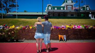 A couple stand in front of flowers outside Dreamworld after the accident in 2016