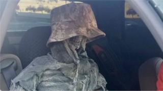 A fake skeleton in a camouflage bucket hat sits in the front of a vehicle in a handout image by the Arizona Department of Public Safety