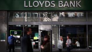 People stand outside or walk past a Lloyds bank branch