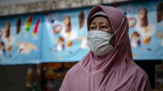 A woman wears a protective mask stands at a local bus station on March 15, 2020 in Yogyakarta, Indonesia.