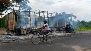 A biker passes by a burned truck on the side of the road in a village near Beoumi on May 17, 2019 after violence erupted between members of the Baoule local community and northern ethnic group Dioula people. Fighting erupted between people of the Baoule and Dioula tribes Wednesday at Beoumi, a town in the centre of the country, after an altercation between a taxi driver and a motorbike taxi operator at a taxi rank, said witness Innocent Koffi, a local farmer. The clashes caused nine deads and 84 injured people including six gendarmes and several houses and vehicles were set ablaze.