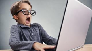 Niño con computadora y cara de asustado.