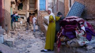 A woman stands in a street with rubble on the floor