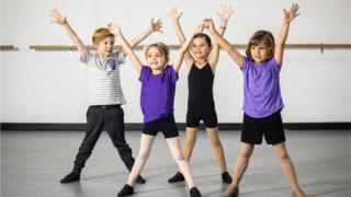 Four children in sports kit with their arms in the air