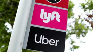 A sign with the logos of Lyft and Uber on a bus stop are seen in this photo