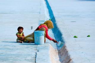 A woman paints the floor of a pond as her child pulls at her sari in Delhi, India