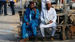 Двое мужчин слушают радио, пока нигерийцы ожидают результатов президентских выборов в Кано, Нигерия, 24 февраля 2019 года.