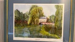 A painting in a photo frame. The painting is of a house, water and trees