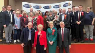 Joy Allen surrounded by supporters wearing a red rosette 