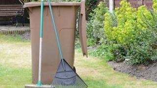 Brown bin in a garden with gardening implements