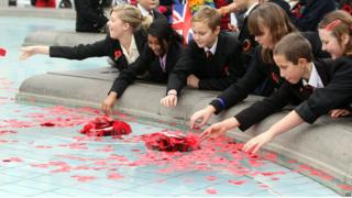 children leaning into fountain to throw poppies in