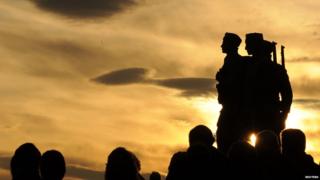 silhouette of war memorial with people gathered beneath it.