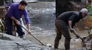 Two men sweeping and digging mud out of the street
