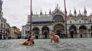 A young man and a woman enjoy swimming in flooded St. Mark's Square in Venice, Italy.