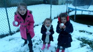 Three girls standing in a snowy garden holding snowballs.