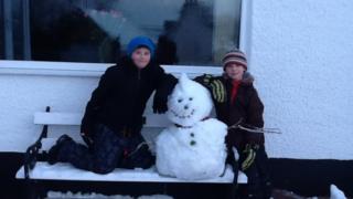 A snowman on a bench with two boys.