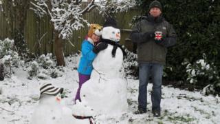 A girl poses beside a snowman, snowdog and snowchild she has built.