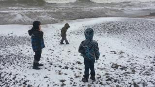 Three boys on a snow covered beach.