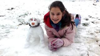 A girl lying in the snow next to a snowdog.