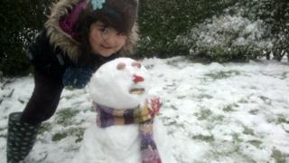 A girl standing beside her snowman.