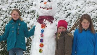 A tall snowman next to three girls.