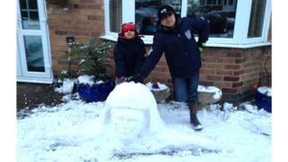 Two boys next to a snow sculpture of a head