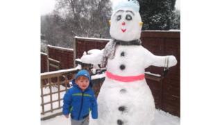 A boy stood next to an enormous snowman.
