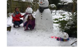 A lady and girl beside a snowlady, snowman and snowcat.