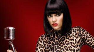 Jessie J in a publicity still for The Voice UK. She is wearing a leopard print top and holding a microphone.