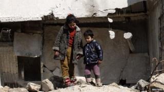 Children in Syria next to war torn buildings