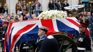 A Union flag draped coffin is carried on a gun carriage drawn by the King's Troop Royal Artillery