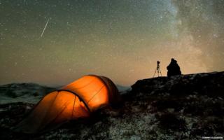 A photographer camping out in a remote location and spending hours waiting for the perfect shot of the night sky.
