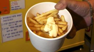 A round pot of vending machine chips. The chips are of the thin French fry variety and are garnished with a dollop of mayonnaise.