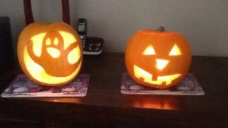 Two pumpkins, one carved with a ghost, the other with a creepy face