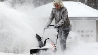 Woman blowing snow away from driveway