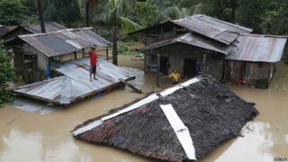 A resident stands on the roof of his home that is submerged in flood water.