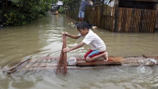 A boy uses a broom to paddle a piece of wood that he is using as a raft along a flooded road in Butuan City.