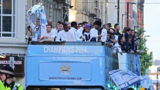 Manchester City team on top of bus holding trophy
