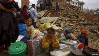 People sitting with their belongings outside a damaged building in Kathmandu.