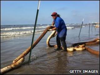 A BP clean-up worker stretches an oil-soaked boom along a beach on Elmer's Island, Louisiana, 23 May