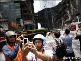 Passers-by take pictures of burned-out buildings in Bangkok on 24 May 2010