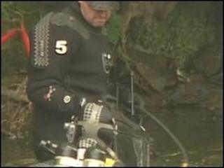 A police diver hands the large, black suitcase to a waiting officer
